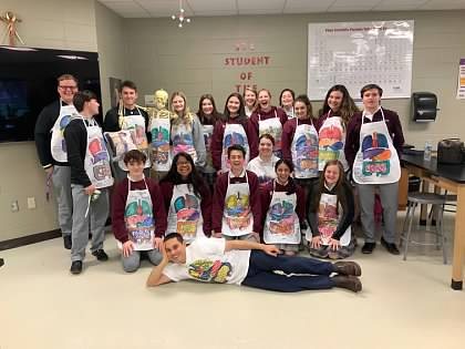 A whole class in anatomy aprons, with Paul lying on the floor in front.