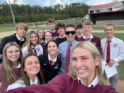Paul in the middle of a big group selfie with students on a baseball field.