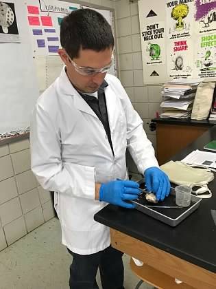 Paul in a white lab coat and safety goggles, working at a lab bench.